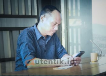 Ketua Desk Pilkada Gerindra Pohuwato, Arfan Dalanggo sedang duduk menggunakan handphone.