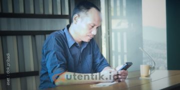 Ketua Desk Pilkada Gerindra Pohuwato, Arfan Dalanggo sedang duduk menggunakan handphone.